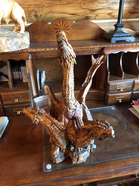 A hand-carved wooden sculpture of a three-headed dragon. The dragon's heads stretch upward with fierce expressions, and the detailed carving highlights the intricate scales and textures of the wood.